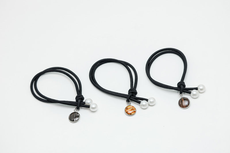 Three black hair ties with two pearls and a lionfish charm on each on a white background.