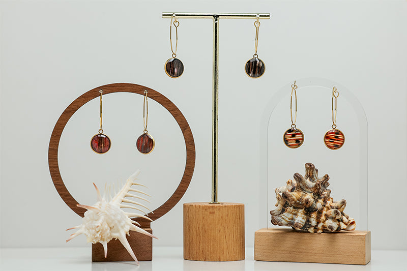 Three pairs of Gold Hexagon Hoops earrings on stands on a white background with two shell at the bottom of the image.