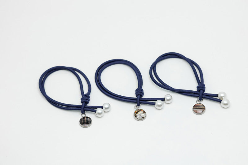 Three blue hair ties with two pearls and a lionfish charm on each on a white background.