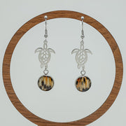 Silver Turtle Dangles on a circular wooden stand on a white background.