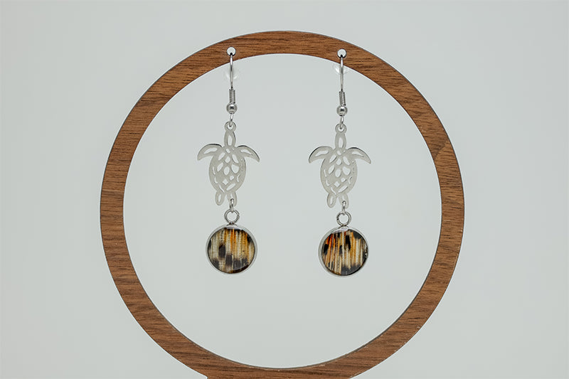 Silver Turtle Dangles on a circular wooden stand on a white background.