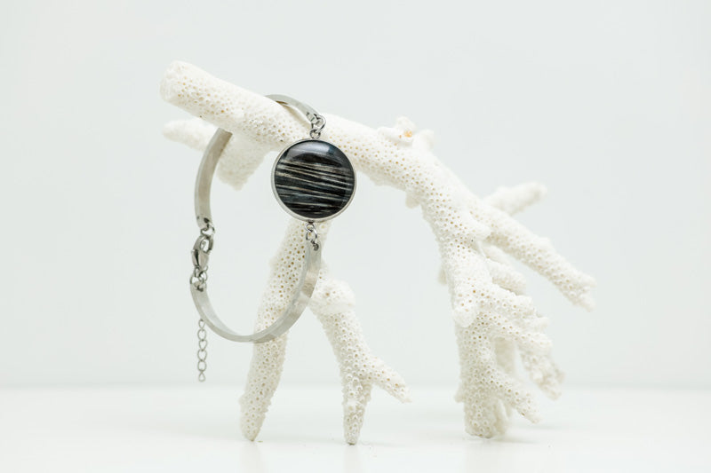 A Round Silver Bracelet hanging from white coral on a white background. 