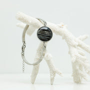 A Round Silver Bracelet hanging from white coral on a white background. 