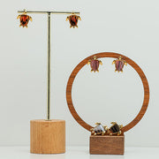 Three pairs of Mini Gold Turtles earrings on stands on a white background.  