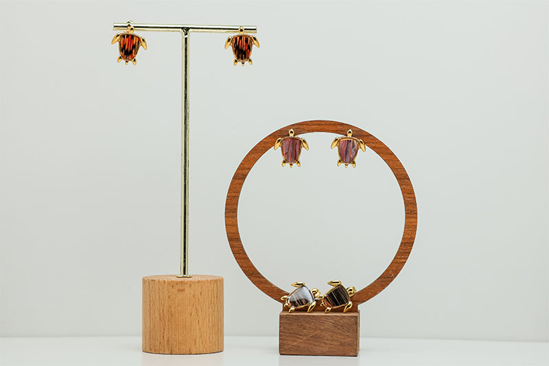 Three pairs of Mini Gold Turtles earrings on stands on a white background.  