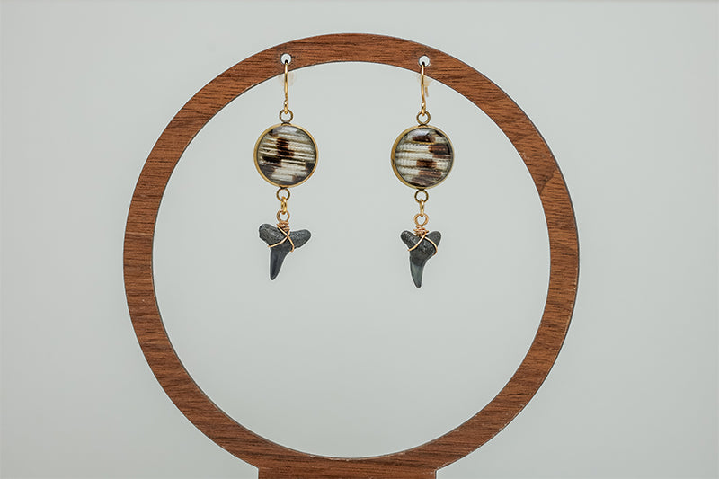 Shark Tooth Gold Dangles Earrings on a circular wooden stand on a white background. 