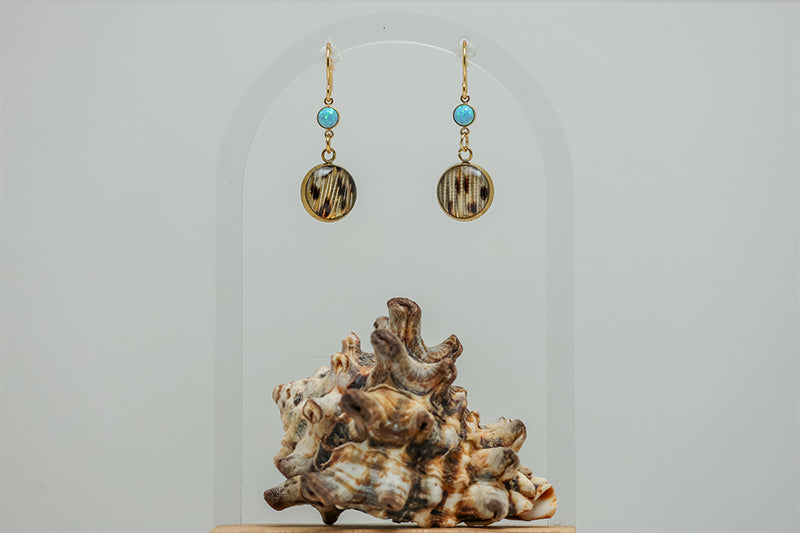 Blue Lagoon Opal Earrings on a white background with a shell at the bottom of the image. 