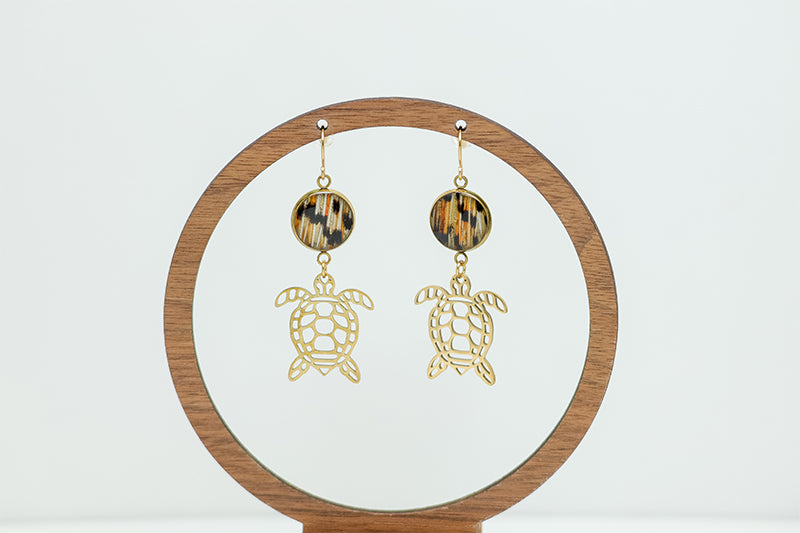 Golden Turtle Earrings on a circular wooden stand on a white background.