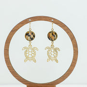 Golden Turtle Earrings on a circular wooden stand on a white background.
