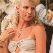 A woman in a cream tube top wearing two bracelets, two necklaces and earrings.