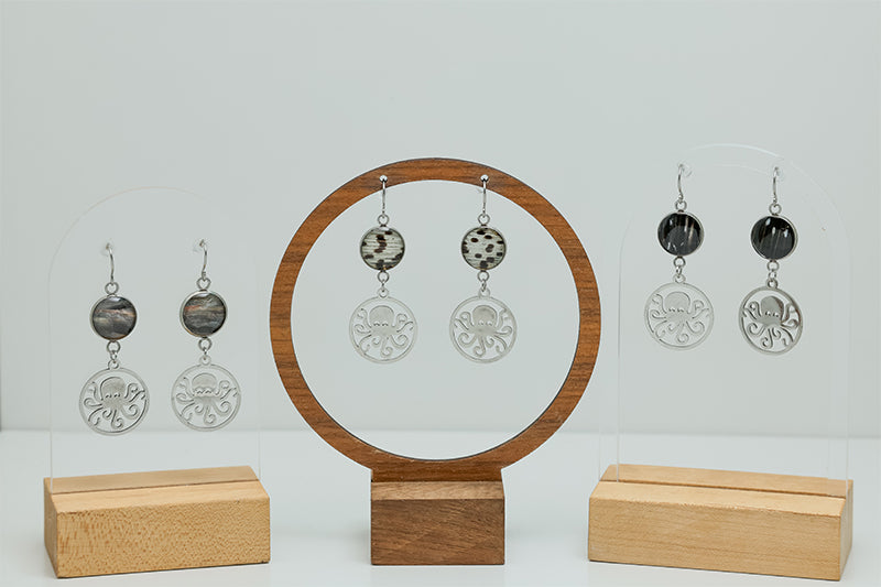 Three pairs of Octopus Earrings on stands on a white background. 