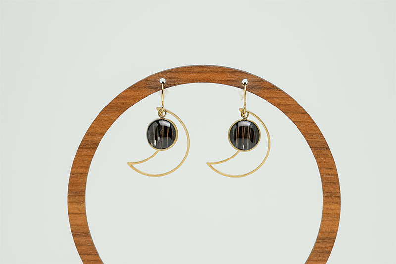 Golden Moon Earrings on a circular wooden earring stand on a white background.  
