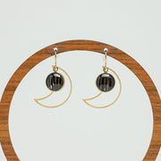 Golden Moon Earrings on a circular wooden earring stand on a white background.  