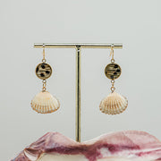 Small Scallop Shell Drops on a gold stand on a white background with a pink clam shell at the bottom of the image.