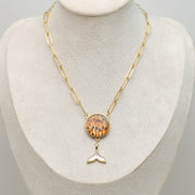 A Whale Tail Necklace on a cream necklace display bust. 