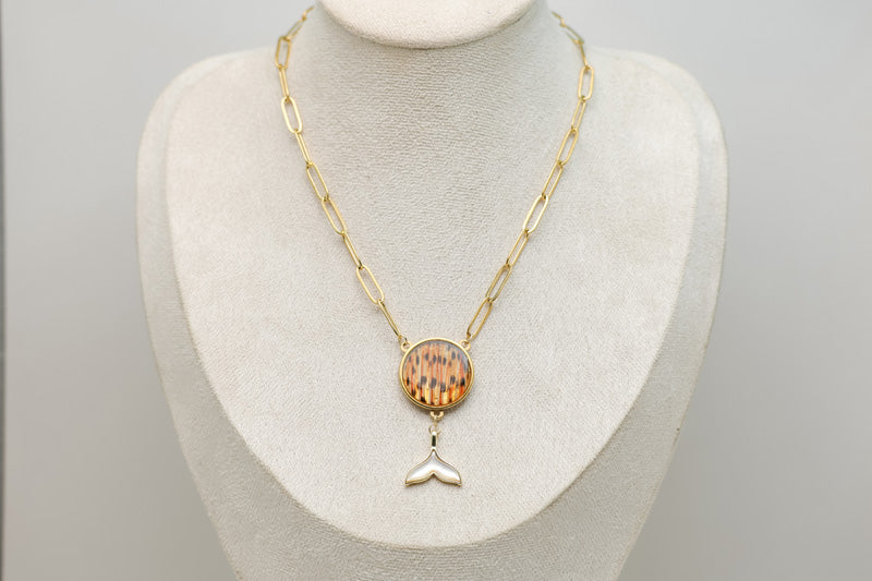 A Whale Tail Necklace on a cream necklace display bust. 