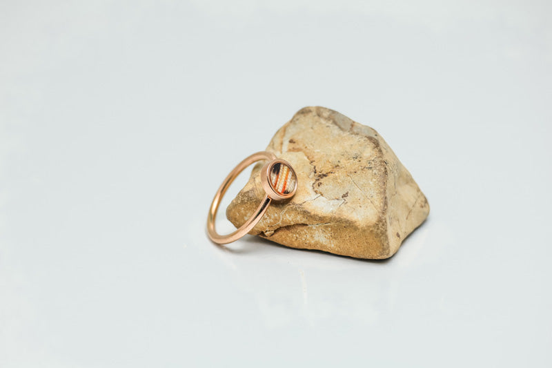 A Mini Rose Gold Ring on a rock on a white background.