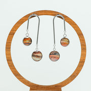 Asymmetrical Bar Earrings on a circular wooden stand on a white background. 