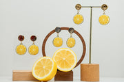 Three pairs of  Limoncello Earrings on stands on a white background with a lemon cut in half at the bottom of the image. 