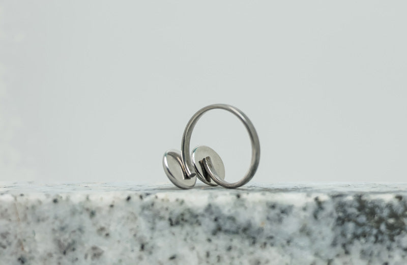 A Silver Double Pendant Adjustable Ring on black and white marble on a white background.
