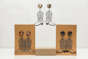 Cowboy boot earrings with lionfish fins displayed on cardboard stands with a white background
