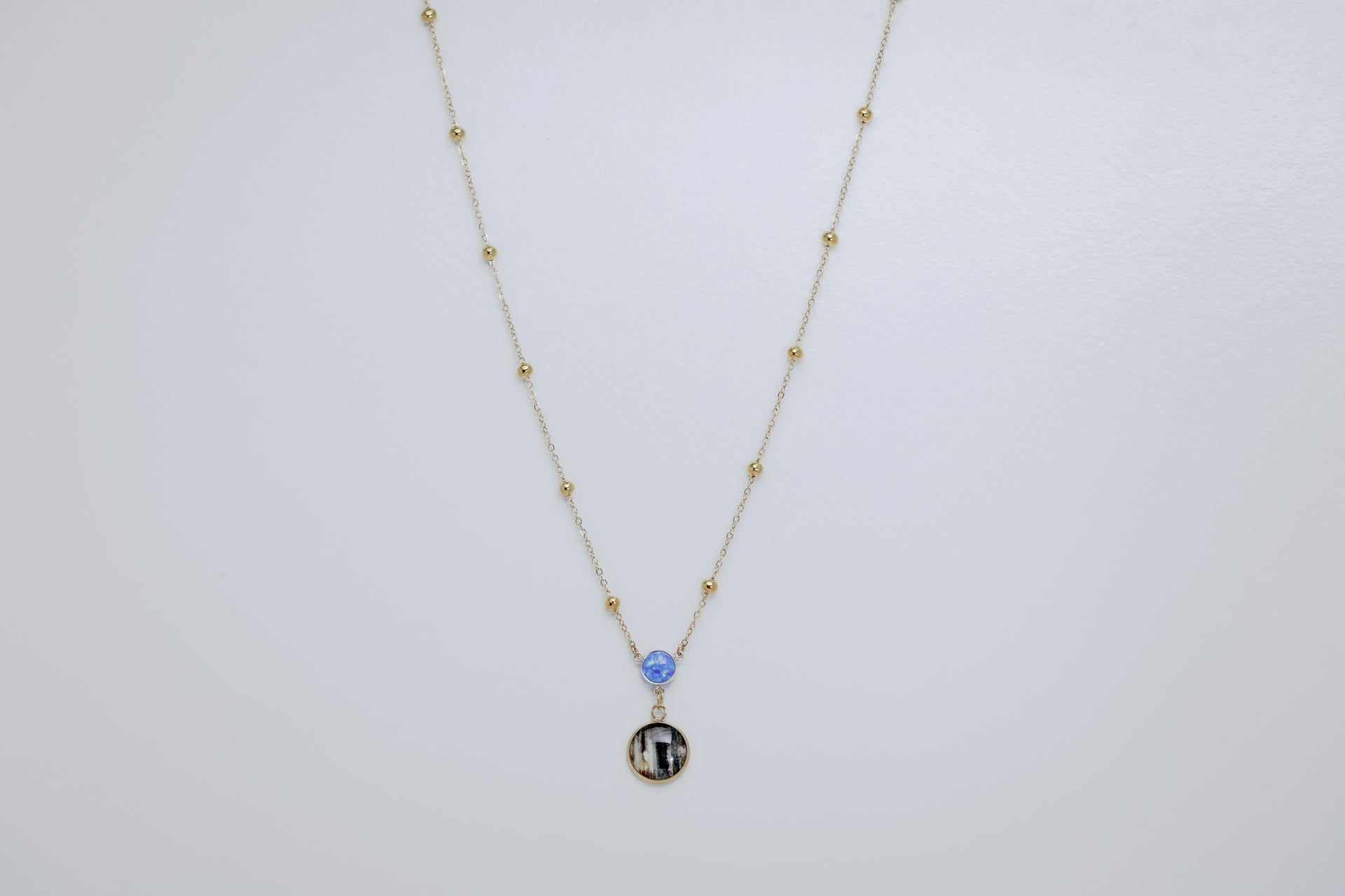Necklace with a lionfish pelvic fin charm and blue opal on a white background