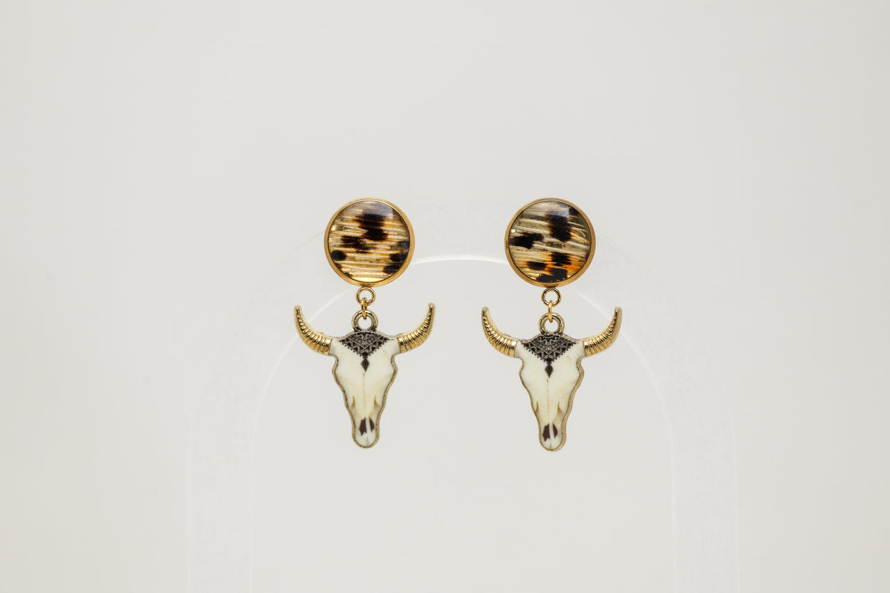 Pair of gold bull skull earrings with lionfish fins on a light gray background