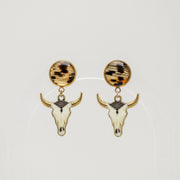 Pair of gold bull skull earrings with lionfish fins on a light gray background