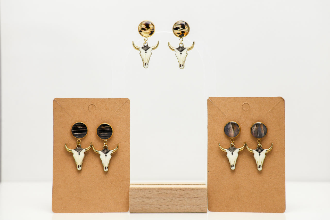 Pair of bull head earrings with lionfish fins on brown card holders against a white background