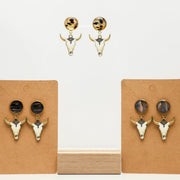 Pair of bull head earrings with lionfish fins on brown card holders against a white background