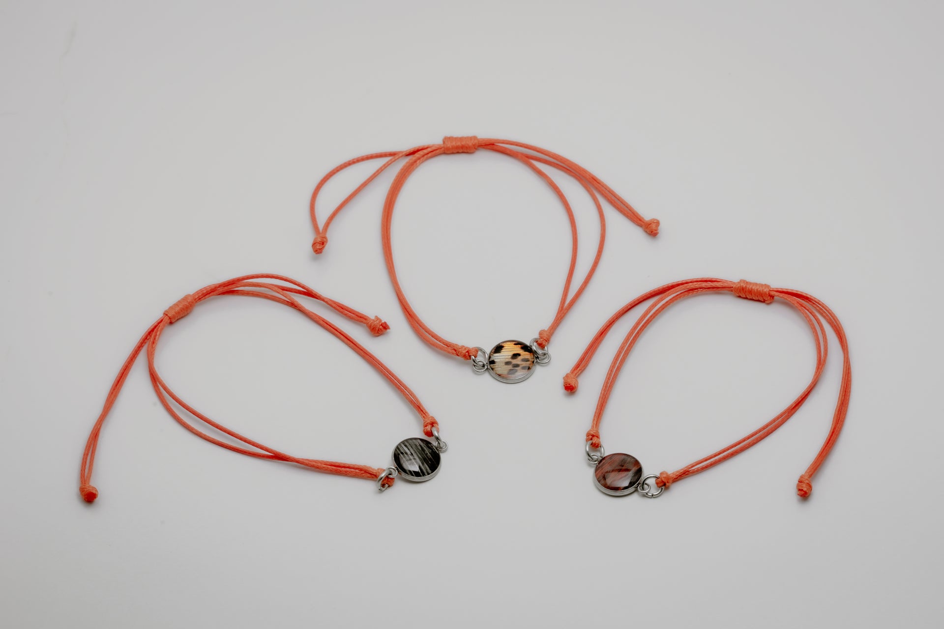 Three orange bracelets with lionfish charms on a light gray background