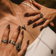 Close-up of hands with dark nail polish and silver jewelry on a neutral background