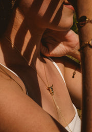 Close-up of a person wearing a gold necklace with a pendant, with sunlight casting shadows.