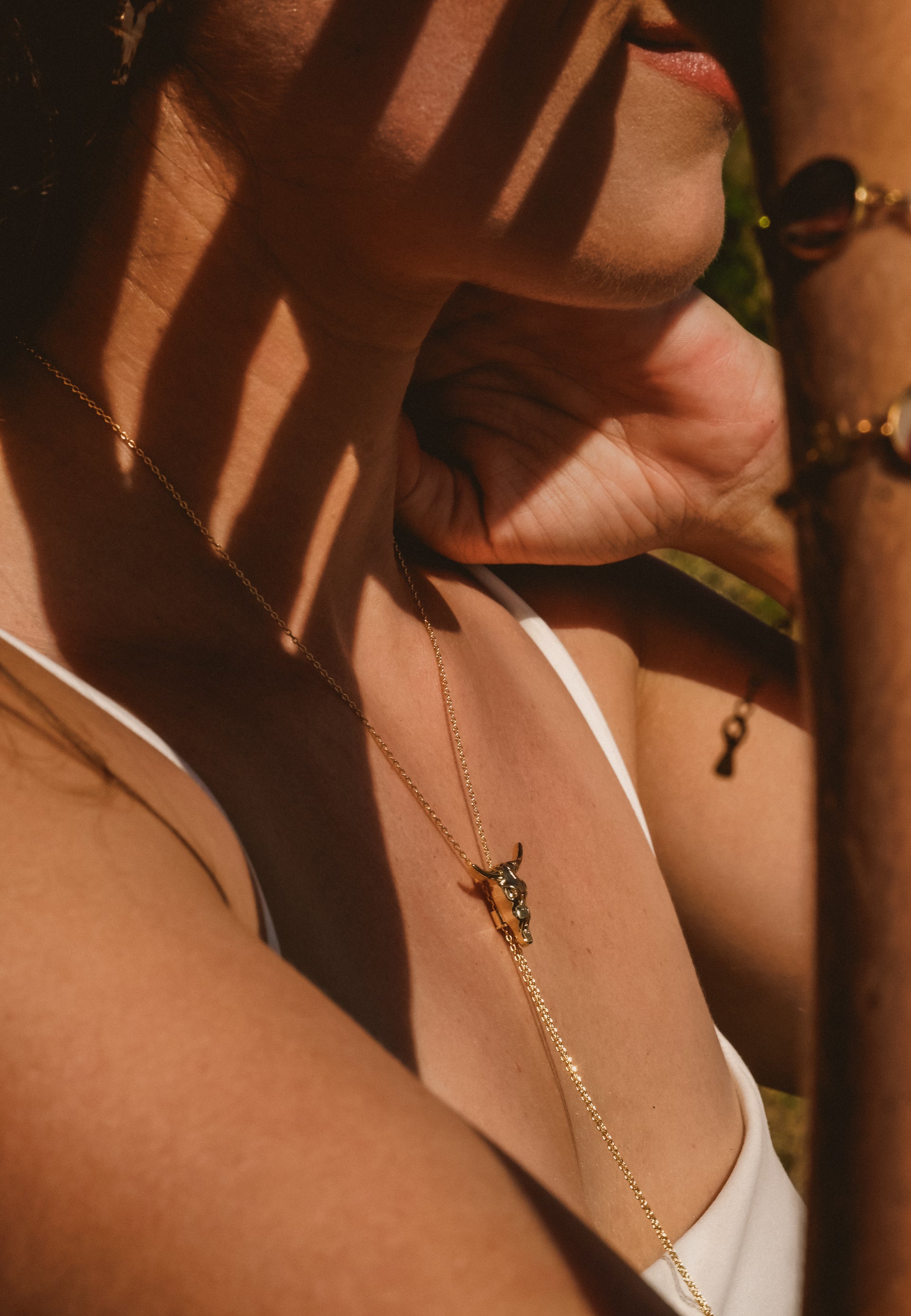 Close-up of a person wearing a gold necklace with a pendant, with sunlight casting shadows.