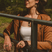 Woman in a cowboy hat and brown jacket standing in a field.
