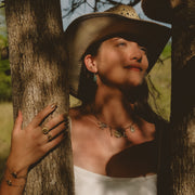 Woman wearing a cowboy hat and white dress, leaning against a tree in a natural setting