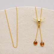 Gold necklace with amber lionfish fins on a display card against a gray background