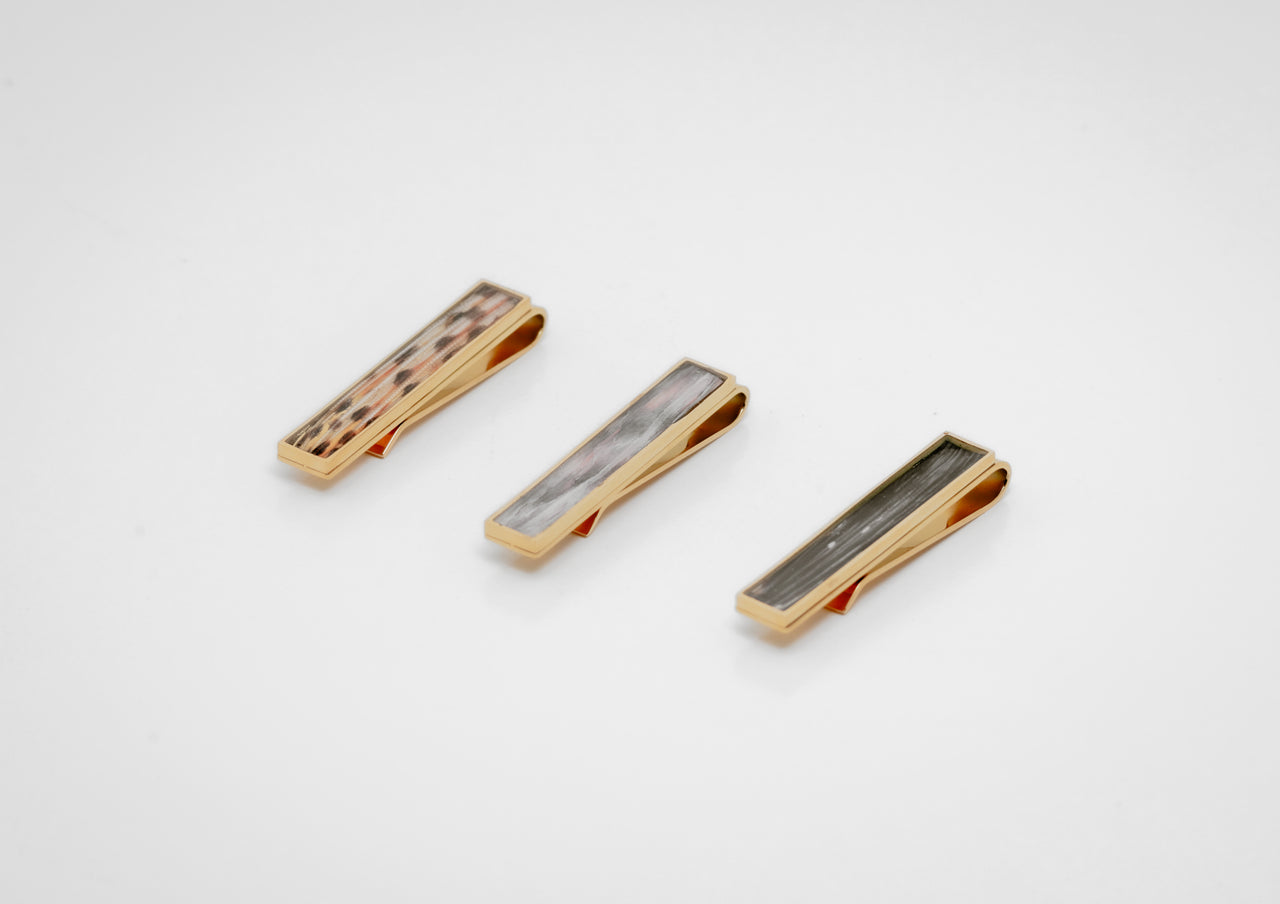 Three gold tie clips with lionfish fin inlay on a white background