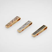 Three gold tie clips with lionfish fin inlay on a white background