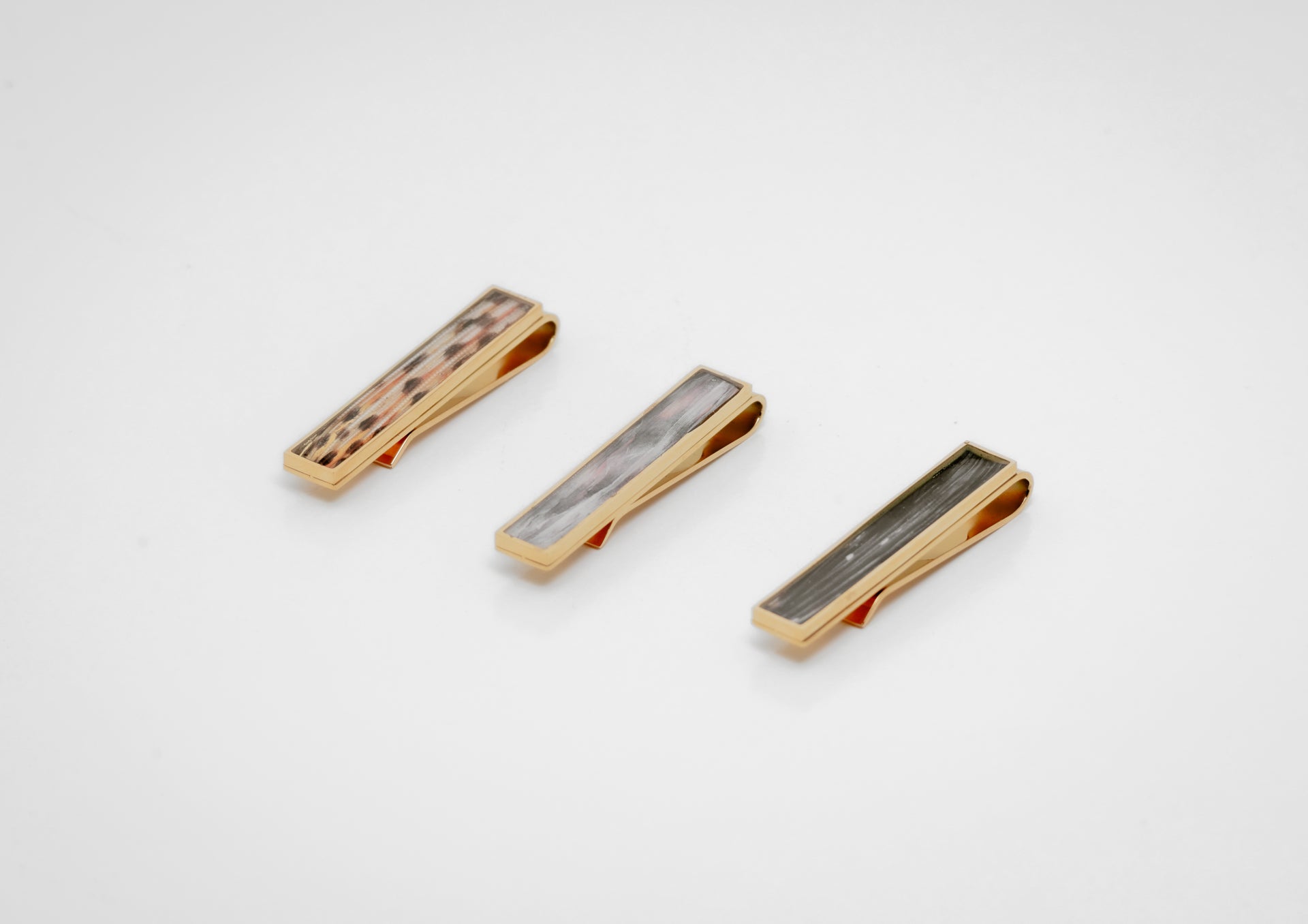Three gold tie clips with lionfish fin inlay on a white background