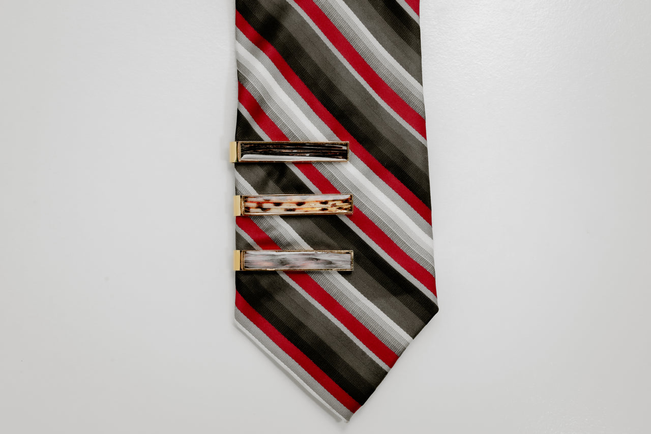 Striped tie with three gold tie clips on a light gray background