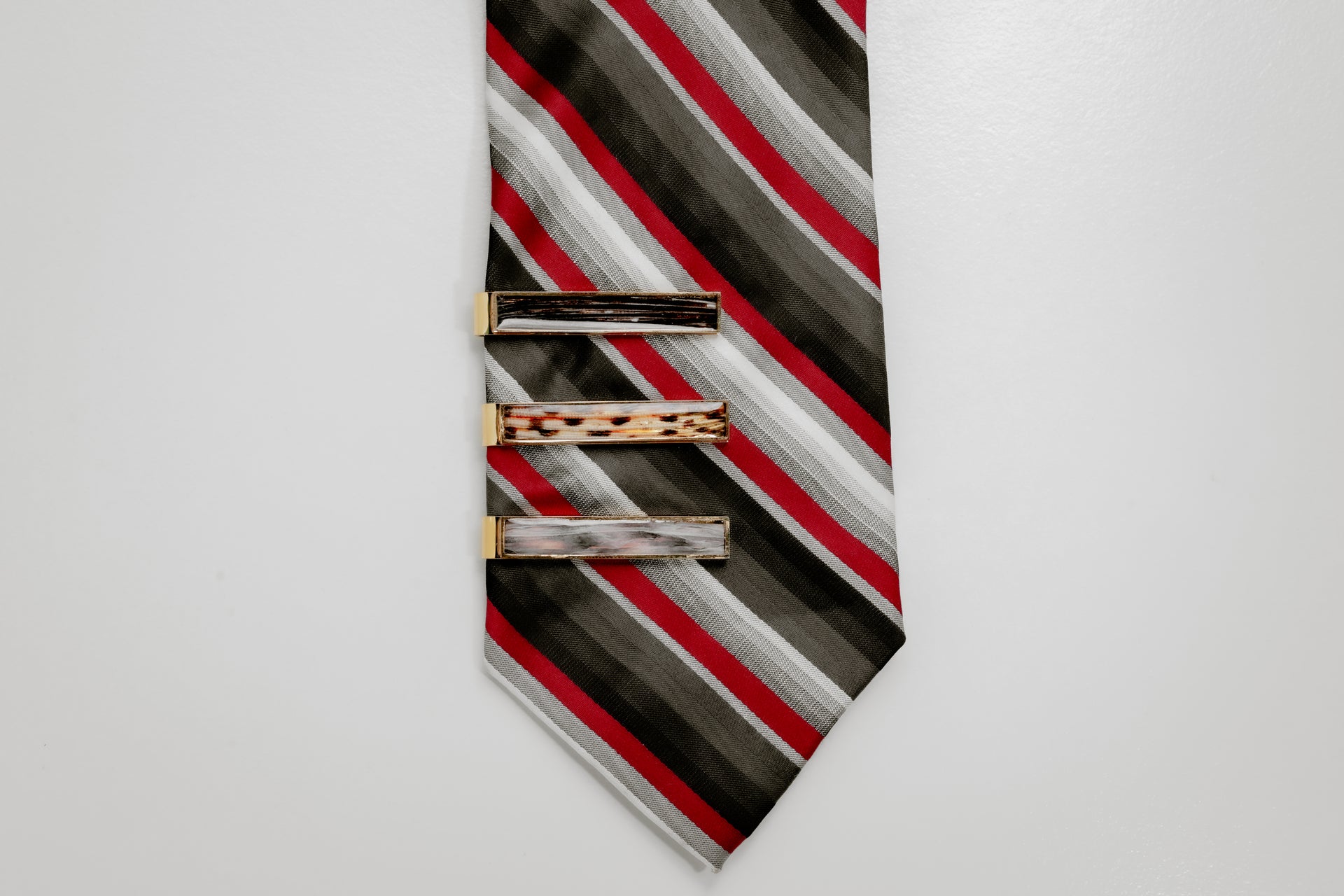 Striped tie with three gold tie clips on a light gray background