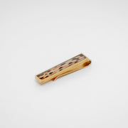 Gold tie clip with lionfish tail fin inlay on a gray background. 