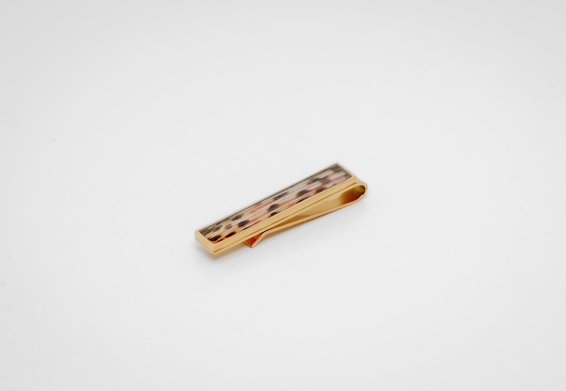 Gold tie clip with lionfish tail fin inlay on a gray background. 