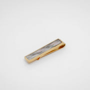 Gold tie clip with lionfish pectoral fin inlay on a gray background. 