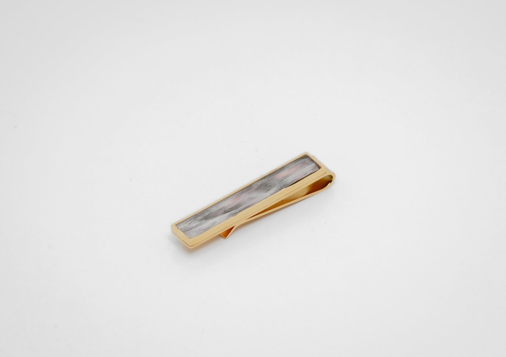 Gold tie clip with lionfish pectoral fin inlay on a gray background. 