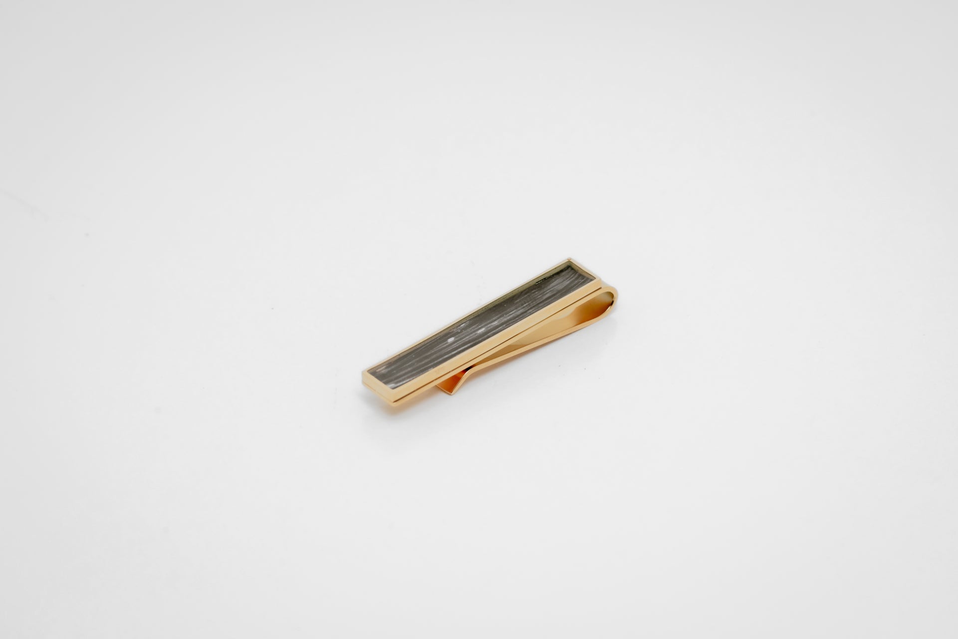 Gold tie clip with lionfish pelvic fin inlay on a gray background. 