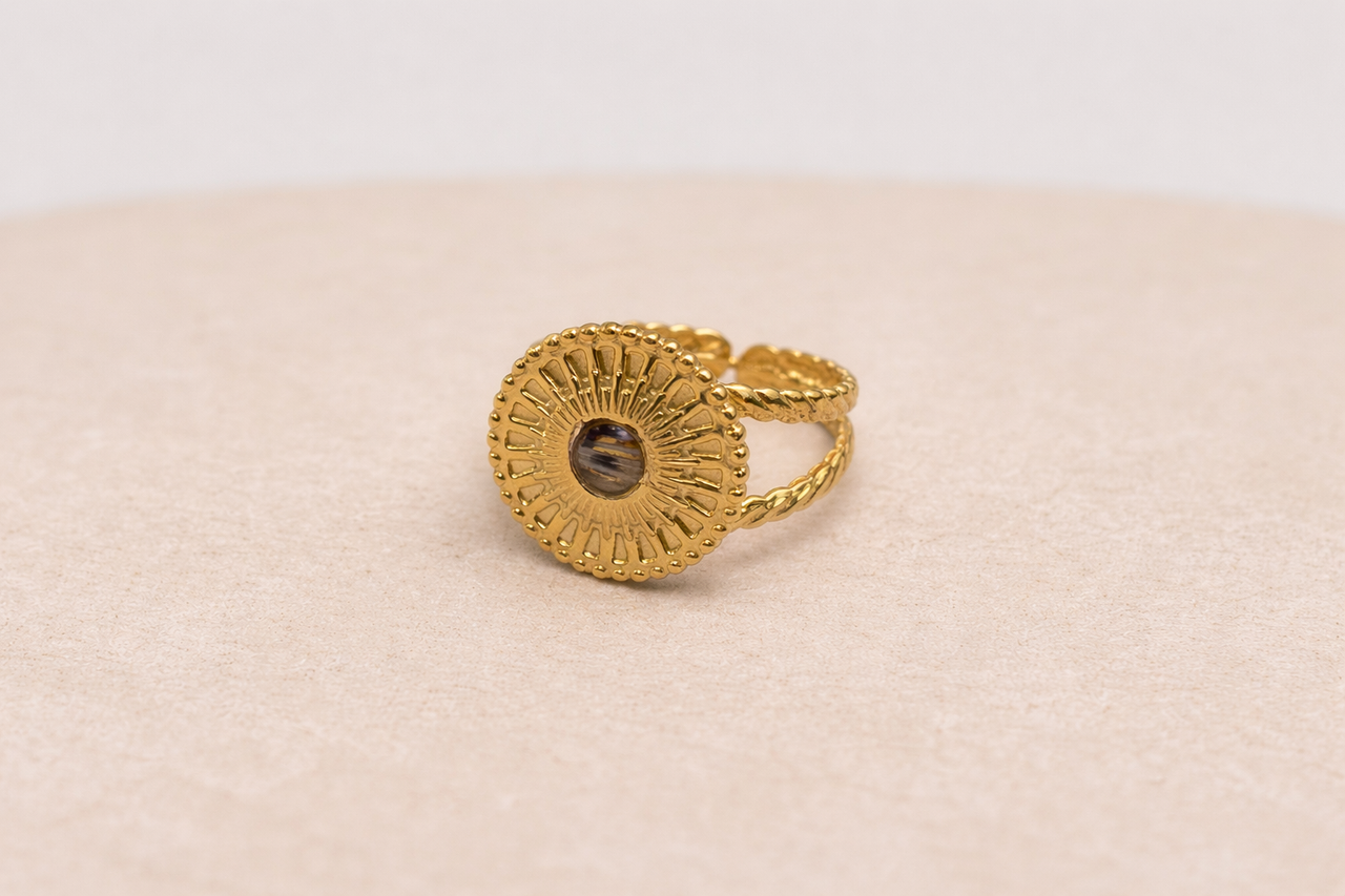 Gold ring with textured design and lionfish fins on a beige fabric background