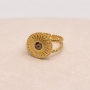 Gold ring with textured design and lionfish fins on a beige fabric background