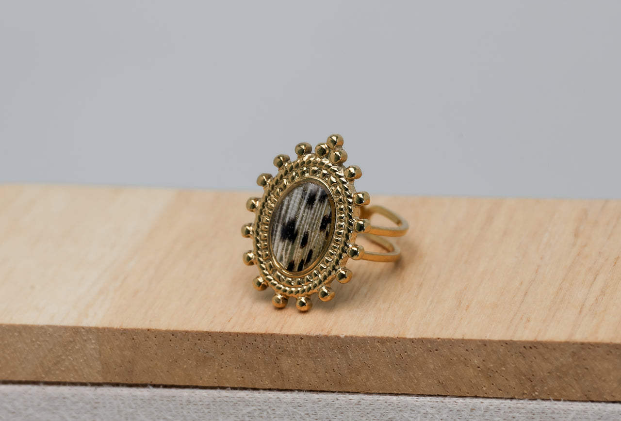 Gold ring with decorative lionfish design on a wooden block against a gray background